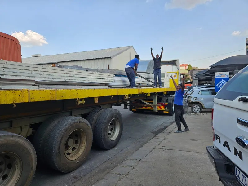 Workers loading structural steel roof sheeting onto a flatdeck trailer